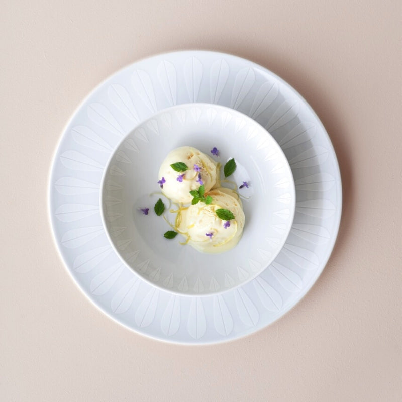 A white plate with a bowl of ice cream and flowers. Servingware with the iconic ‘Lotus’ pattern by Arne Clausen. ARNE CLAUSEN COLLECTION.