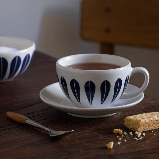 An image of a cup of tea and a biscuit on a table. The servingware features the iconic ‘Lotus’ pattern by Arne Clausen. ARNE CLAUSEN COLLECTION, Lotus | cups, Bowls & plates.
