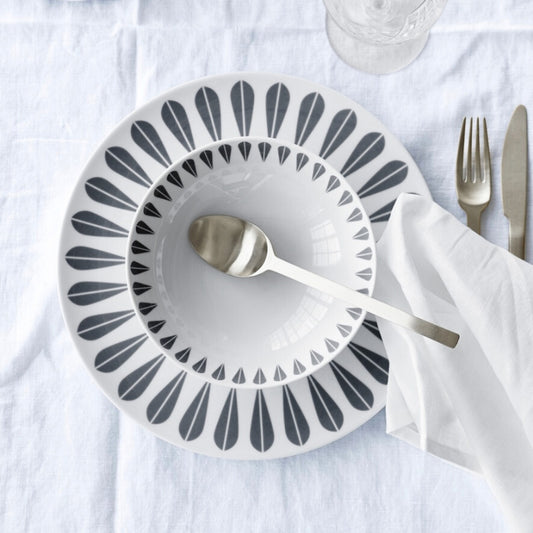 A white table with a black and white plate and silverware. Servingware with the iconic ‘Lotus’ pattern by Arne Clausen.